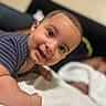 Thiago is registered to the contest to win money with this photo: adorable, baby, bed, blanket, blurred_background, child, close_up, eyes, face, family, happy, indoor, infant, lying_down, open_mouth, playful, portrait, short_hair, smiling, striped_shirt