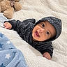 baby, baby_clothing, bed, blanket, blue_blanket, child, cozy, eyes, face, happy, hood, hoodie, indoor, infant, lying_down, photography, portrait, smiling, stuffed_animal, teddy_bear