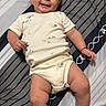 baby, child, infant, smiling, portrait, lying_down, bed, bedspread, striped, onesie, clothing, happy, face, eyes, arms, legs, bracelet, indoor, cozy, photography