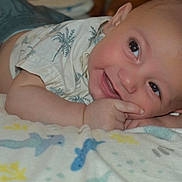 Apollo joined the competition — help win amazing prizes! baby, infant, smile, face, hand, blanket, pattern, blue, yellow, clothing, toddler, skin, cute, lying_down, cheeky, indoors, happy, closeup, person, child
