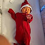 Jackson joined the competition — help win amazing prizes! baby, infant, red_onesie, santa_hat, pointing, winking, lying_down, cozy, holiday, festive, smiling, cute, newborn, bed, soft_lighting, sleepwear, indoor, person, celebration, child