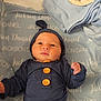 baby, newborn, infant, blue_outfit, blanket, wooden_sign, birth_announcement, buttoned_clothing, lying_down, bed, hospital, cute, child, person, face, headwear, swaddled, sleepwear, indoors, soft_lighting