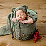 newborn, baby, sleeping, knitted_hat, bear_ears, bucket, blanket, wooden_floor, decorative, berries, cozy, infant, portrait, cute, resting, soft_texture, wrapped, small, peaceful, indoors