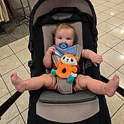 Charles joined the competition — help win amazing prizes! baby, child, stroller, pacifier, plush_toy, orange, blue, indoor, floor_tiles, curious, legs, bib, seat, shopping_area, cute, infant, person, toy, casual, holding