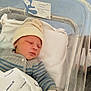 newborn, baby, sleeping, hospital, bassinet, blanket, hat, clothing, infant, person, indoors, bed, pale_skin, blue_floor, white_gloves, knitwear, portrait, peaceful, resting, hospital_bed