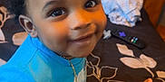 Dekhari joined the competition — help win amazing prizes! toddler, child, smiling, blue_shirt, bed, bedding, floral_pattern, wooden_headboard, indoor, person, skin, hand, foot, face, eyes, hair, necklace, happy, sitting, home