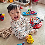 Ewen a rejoint le concours — aidez-le/la à gagner de superbes lots ! toddler, child, smiling, toy, toy_truck, floor, pajamas, animal_print, indoor, playtime, happy, colorful, plastic_toy, vehicle_toy, chair, blanket, curtain, window, person, casual