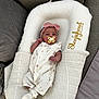 baby, infant, pacifier, headband, pink_bow, sleepyhead_deluxe, blanket, couch, soft_fabric, white_clothing, floral_pattern, socks, newborn, resting, indoors, cozy, comfort, child, cute, portrait