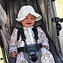baby, child, stroller, hat, smile, happy, outdoor, sunlight, clothing, safety_harness, infant, seat, fabric, pattern, person, cute, baby_clothes, headwear, baby_boy, daylight