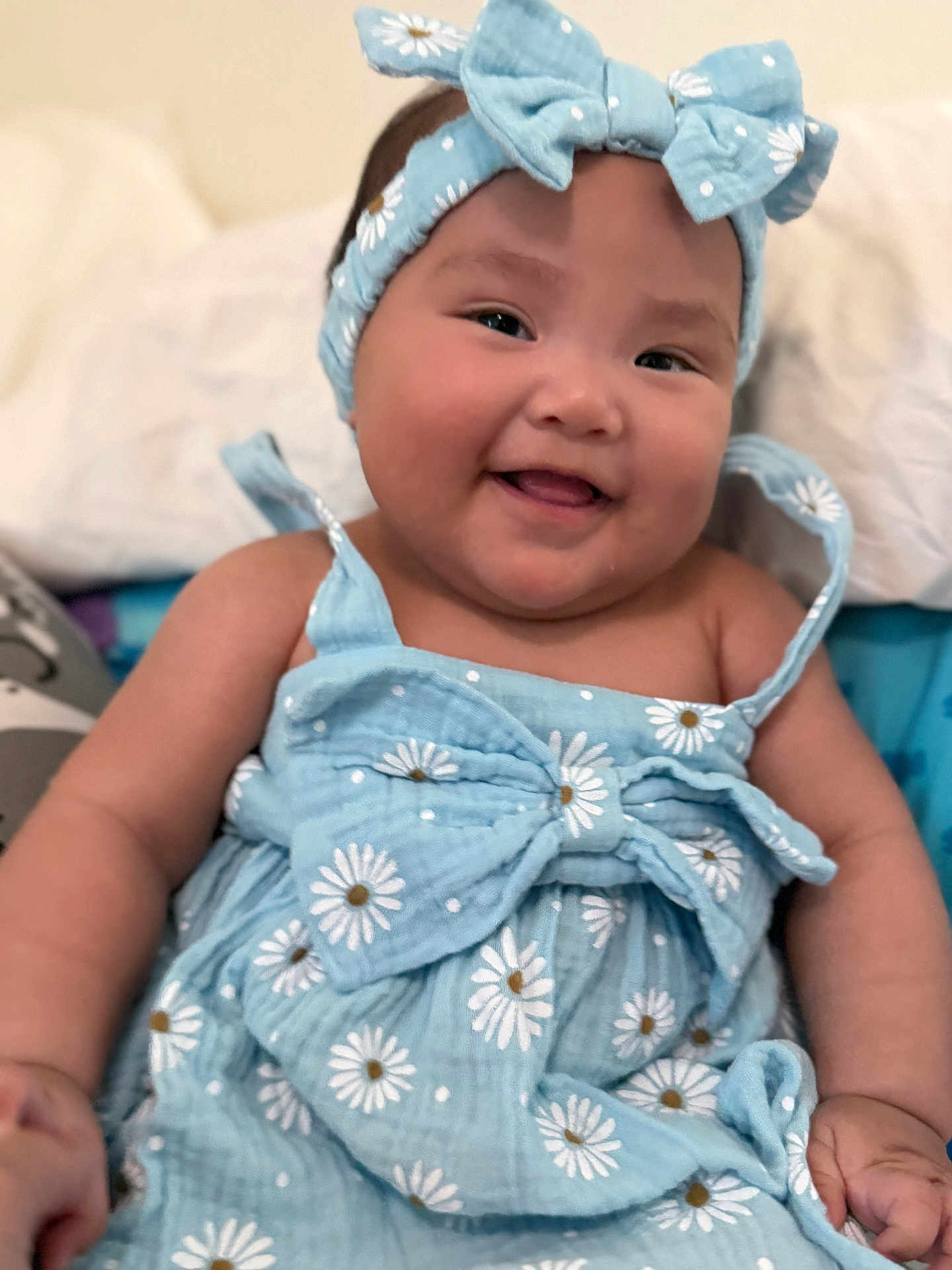 Athena is registered to the contest to win money with this photo: baby, child, smiling, blue_dress, headband, daisy_pattern, cute, happy, portrait, infant, cheeks, clothing, sitting, indoors, human, person, cute_outfit, joyful, closeup, adorable