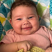 Ember joined the competition — help win amazing prizes! baby, infant, smiling, blanket, knitted, cushion, patterned, colorful, face, cheeks, happy, hand, pink_clothing, portrait, indoors, cute, child, young, resting, cozy