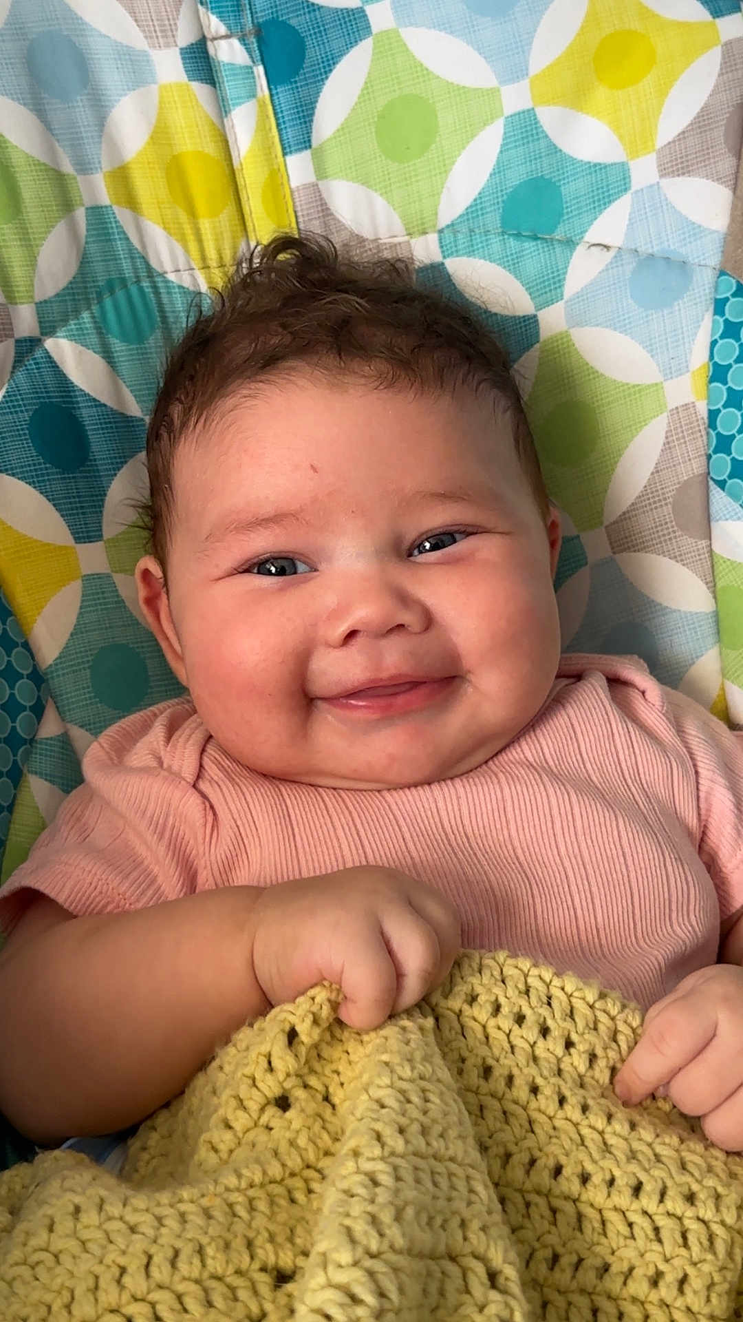 Ember joined the competition — help win amazing prizes! baby, infant, smiling, blanket, knitted, cushion, patterned, colorful, face, cheeks, happy, hand, pink_clothing, portrait, indoors, cute, child, young, resting, cozy
