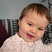 Rosie joined the competition — help win amazing prizes! baby, smiling, face, child, person, pink_clothing, patterned_fabric, cushion, indoor, portrait, happy, cute, young_child, head, cheeks, eyes, mouth, sitting, cozy, home