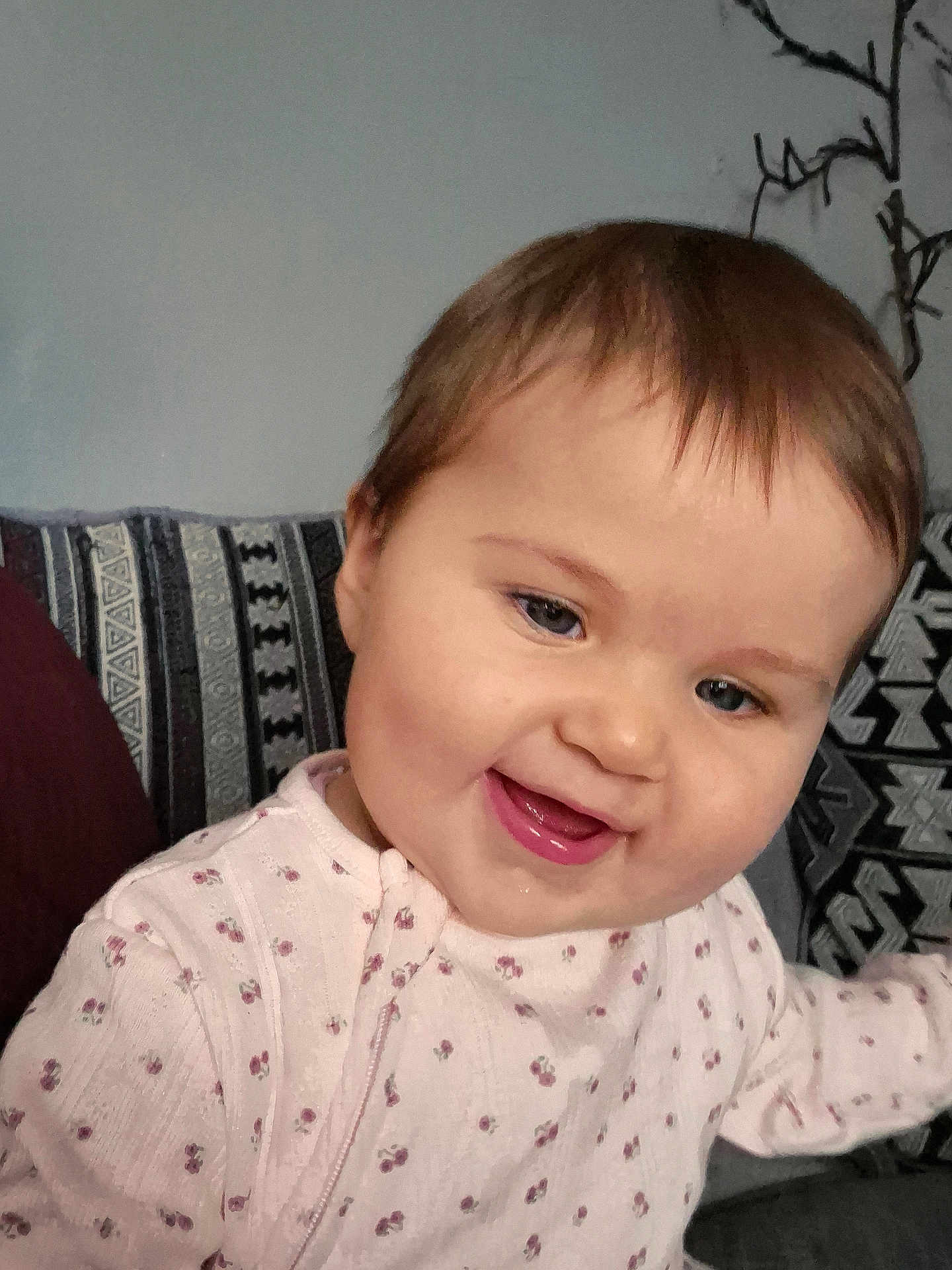 Rosie joined the competition — help win amazing prizes! baby, smiling, face, child, person, pink_clothing, patterned_fabric, cushion, indoor, portrait, happy, cute, young_child, head, cheeks, eyes, mouth, sitting, cozy, home