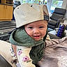 baby, child, smiling, cap, green_vest, indoor, furniture, window, person, happy, portrait, clothing, sitting, modern, hand, face, cozy, casual, light, cute