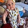 baby, infant, child, person, headband, pineapple_pattern, clothing, bedroom, blanket, hand, face, blue_eyes, tattoo, sitting, comfort, indoor, furniture, door, foot, casual