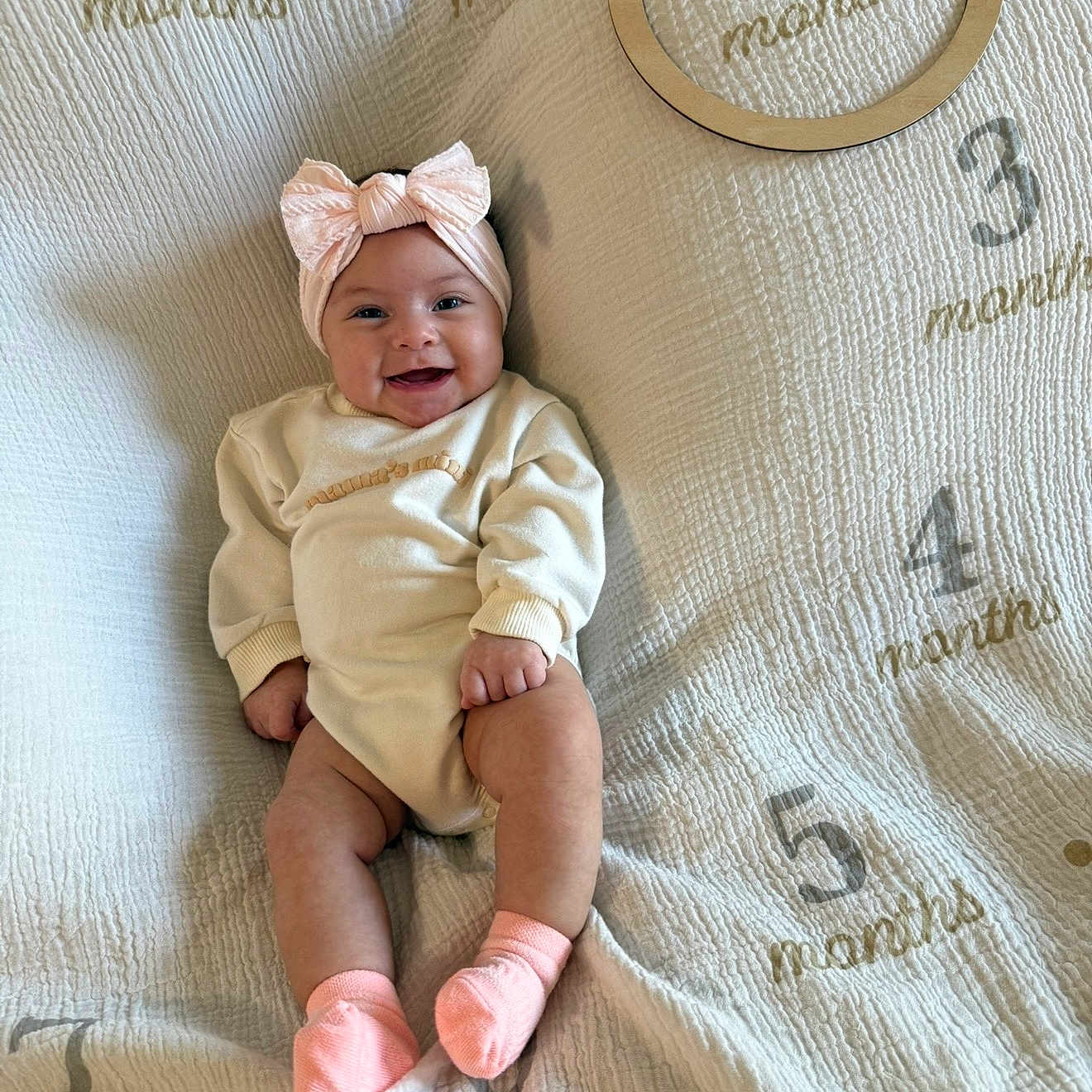 Riella is registered to the contest to win money with this photo: baby, infant, smile, headband, pink_socks, blanket, months_marker, wooden_ring, cute, happy, sitting, child, clothing, portrait, indoors, soft_texture, milestone, young_child, face, celebration