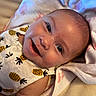 baby, smile, face, infant, pineapple_pattern, clothing, blanket, skin, cute, happy, lying_down, closeup, child, adorable, head, person, soft_texture, cheerful, young, sleepwear