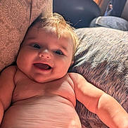 Knox is registered to the contest to win money with this photo: baby, smiling, happy, infant, cute, skin, face, arm, pillow, blanket, indoors, natural_light, child, portrait, closeup, comfortable, relaxed, couch, warm, expression