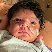 Shay is registered to the contest to win money with this photo: baby, infant, face, curly_hair, nasal_tube, hospital, medical_equipment, polka_dot_clothing, newborn, person, skin, eyes, hand, healthcare, patient, indoors, closeup, care, lying_down, adult_hand