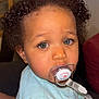toddler, child, pacifier, curly_hair, blue_eyes, indoor, portrait, cute, baby, clothing, sitting, face, person, couch, furniture, closeup, expression, young_child, comfort, soft_lighting