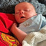 Rylie is registered to the contest to win money with this photo: baby, sleeping, blanket, blue_clothing, red_clothing, manchester_united_logo, soft_texture, face, infant, resting, cozy, cute, crown_embroidery, hand, indoors, person, closeup, peaceful, young_child, comfort