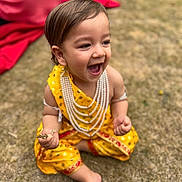Nirvair is registered to the contest to win money with this photo: toddler, child, smiling, yellow_clothing, traditional_dress, pearls, grass, outdoor, happy, laughing, barefoot, sitting, hands, face, young_child, nature, daylight, cute, joyful, playful