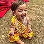 toddler, child, smiling, yellow_clothing, traditional_dress, pearls, grass, outdoor, happy, laughing, barefoot, sitting, hands, face, young_child, nature, daylight, cute, joyful, playful