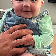 Remi joined the competition — help win amazing prizes! baby, child, smiling, headband, bow, denim_overalls, hand, adult_hand, indoor, skin, face, cute, chubby_cheeks, sitting, clothing, person, infant, happy, portrait, young