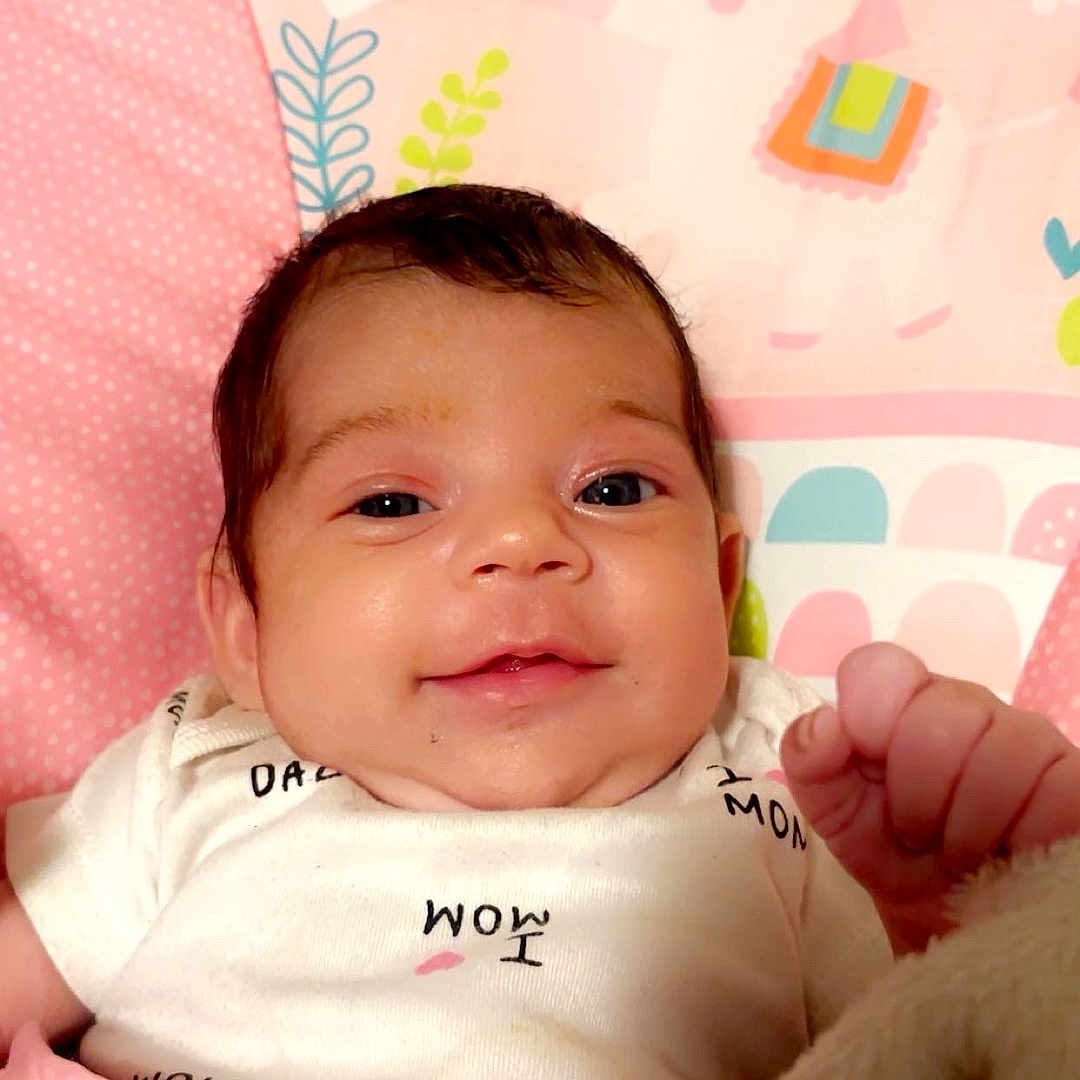 Imari joined the competition — help win amazing prizes! baby, infant, child, portrait, smiling, awake, face, hand, fist, pink, unicorn, blanket, crib, bedding, clothing, onesie, indoor, close_up, happy, cute