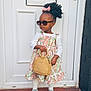 toddler, child, dress, sunglasses, handbag, door, footwear, standing, fashion, curly_hair, bow, white_top, patterned_clothing, tiles, outdoor, person, accessory, confident, portrait, steps