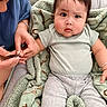 adult_hand, baby, blanket, child, closeup, clothing, couch, curious_expression, face, gray_pants, green_blanket, hand, indoor, infant, jewelry, manicure, nail_clippers, person, seated, skin