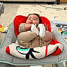 baby, baby_seat, blanket, bracelet, carpet, child, clothing, comfort, couch, cozy, cushion, face, feet, footwear, indoors, infant, living_room, person, playful, toy