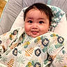 baby, baby_chair, bib, child, clothing, cushion, cute, face, hair, happy, indoors, infant, leaf_pattern, lion_pattern, playful, portrait, seated, skin, smiling, young_child