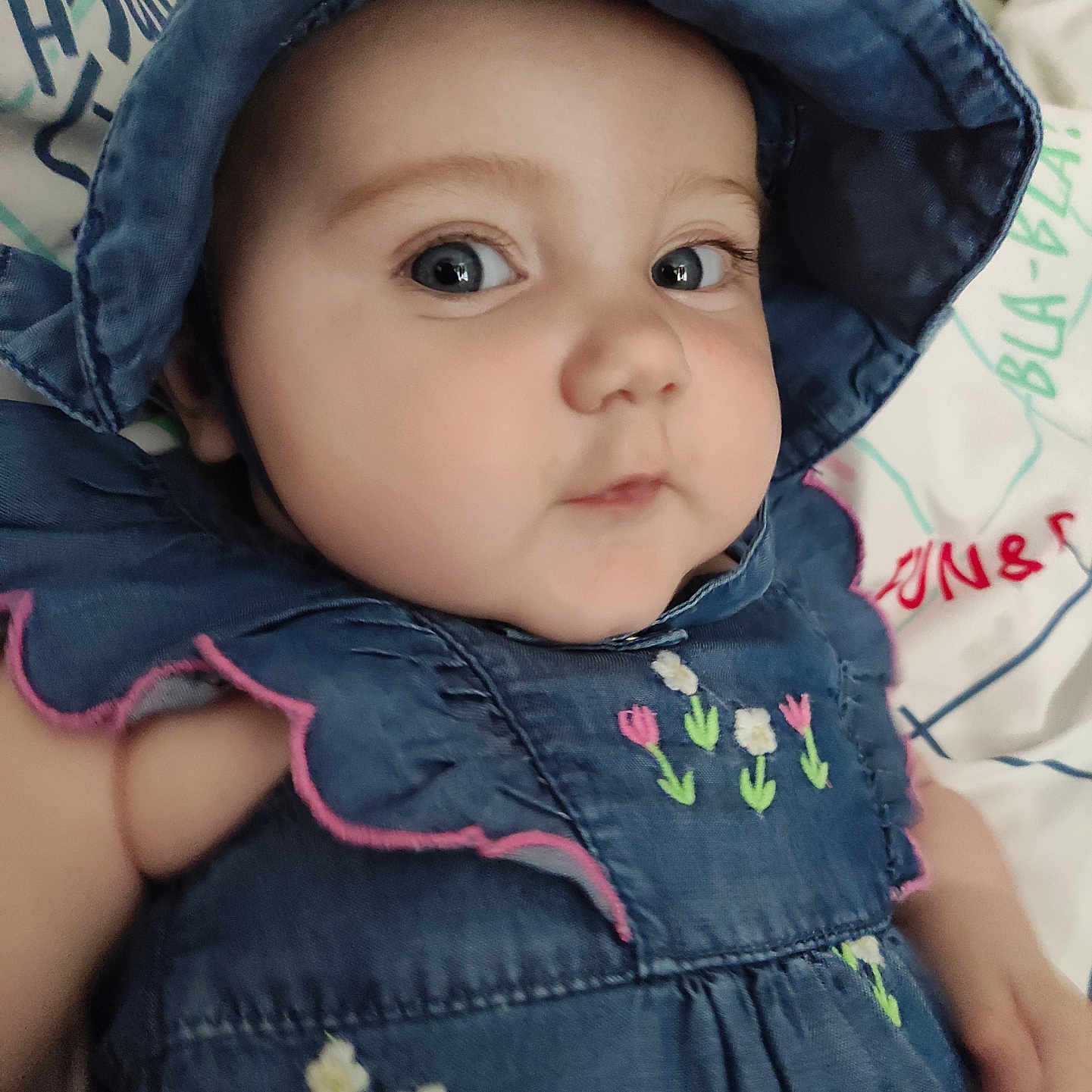 Kalista a rejoint le concours — aidez-le/la à gagner de superbes lots ! baby, blue_hat, cheeks, child, closeup, clothing, cute, denim_dress, embroidery, eyes, face, floral_pattern, hat, indoor, infant, lying_down, person, portrait, skin, young_child