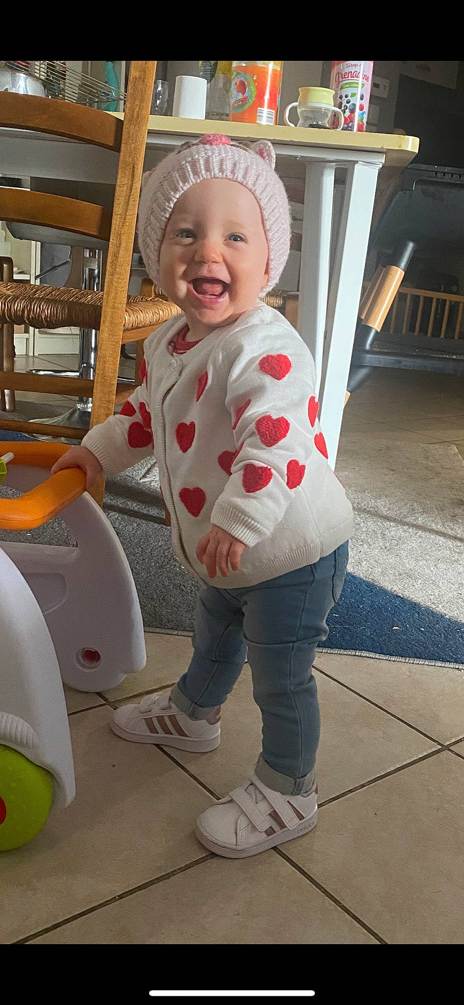 élise a rejoint le concours — aidez-le/la à gagner de superbes lots ! baby, baby_laughing, baby_toddler_clothing, chair, child, floor, flooring, fun, happy, headwear, leg, people, person, pink, riding_toy, sitting, skin, sleeve, smile, sneakers