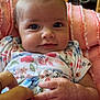Violet joined the competition — help win amazing prizes! baby, infant, hand, finger, blanket, floral_outfit, pink, couch, furniture, television, wood, person, face, skin, eyes, smile, indoors, cozy, cute, home