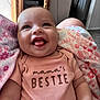 baby, smiling, infant, onesie, blanket, floral_pattern, happy, cute, tongue_out, person, child, indoors, home, arm, clothing, face, head, seated, cozy, soft