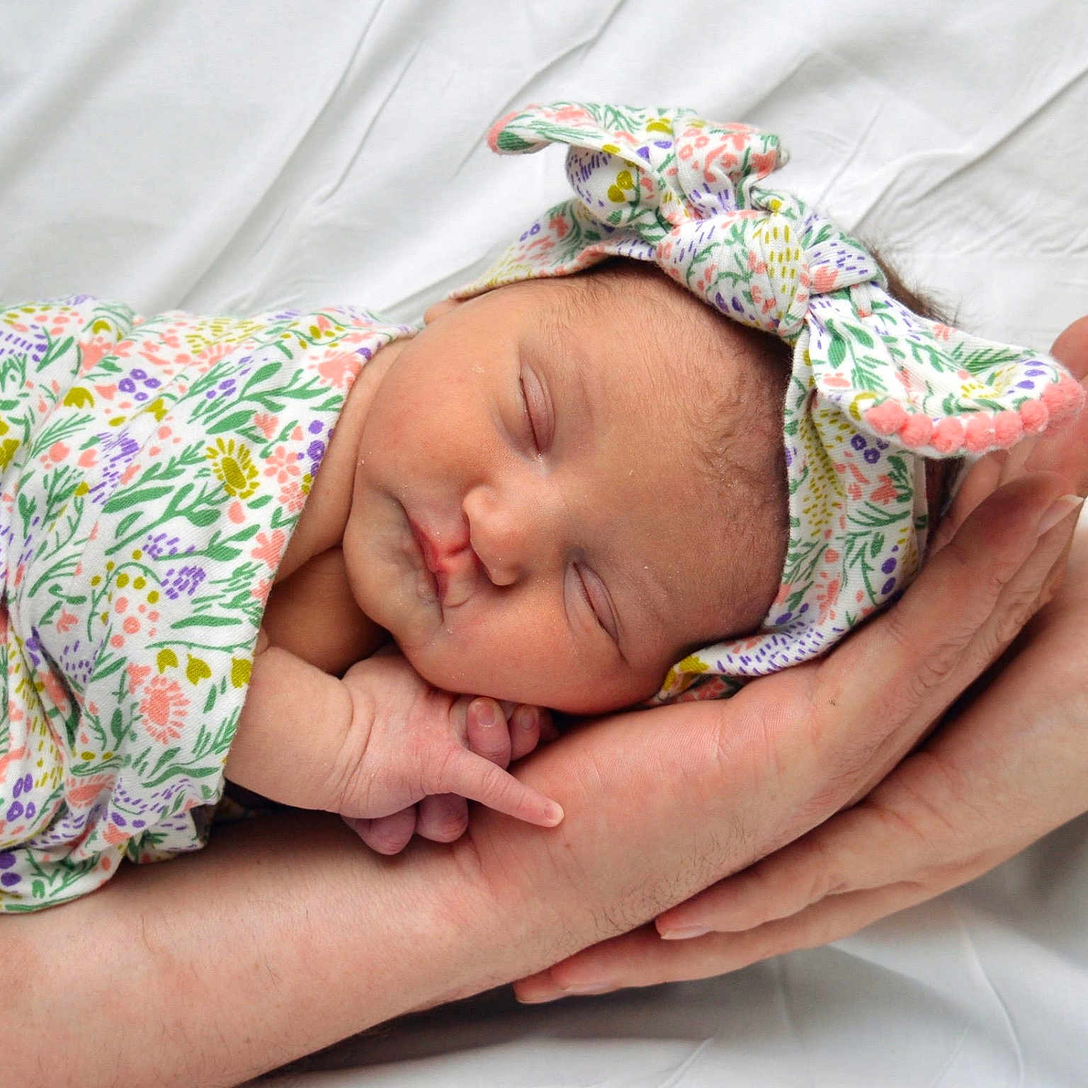 Ariaya Grace joined the competition — help win amazing prizes! newborn, baby, sleeping, infant, portrait, close_up, floral_clothing, hat, hands, adult, cradled, peaceful, indoors, white_bedding, blanket, soft_lighting, family, tender, resting, photography