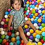 child, girl, ball_pit, colorful_balls, pigtails, yellow_shoes, floral_dress, playground, happy, smiling, indoor, toys, fun, casual_clothing, cute, leisure, portrait, young_child, play, childhood