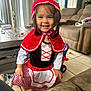 toddler, child, smiling, costume, red_hood, indoor, living_room, toy, sofa, table, curtain, floor_tile, happy, girl, dress, cape, playtime, cute, person, portrait