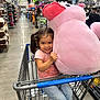 Hazelyn is registered to the contest to win money with this photo: child, girl, shopping_cart, plush_toy, pink, toy, store, aisle, shopping, casual_clothing, jeans, pigtails, smiling, retail, indoor, floor, yellow_shoes, metal_cart, person, happy