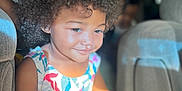 Dakota is registered to the contest to win money with this photo: child, toddler, curly_hair, afro, smiling, colorful_dress, floral_pattern, sunlight, car_interior, seat, hand, portrait, happy, cute, person, indoors, daylight, skin, young_child, people