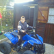 Dylan a rejoint le concours — aidez-le/la à gagner de superbes lots ! child, children, atv, blue_vehicle, outdoor, garden, wooden_shed, grass, flag, toy, play, casual_clothing, daylight, fun, yard, greenery, vehicle, boy, young, leisure