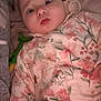 Sienna is registered to the contest to win money with this photo: baby, infant, child, onesie, floral_pattern, bed, blanket, toy, lying_down, curious_expression, face, skin, head, hand, comfort, soft, indoor, cute, young, person