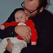 Jimmy joined the competition — help win amazing prizes! baby, man, holding, glasses, beard, red_clothing, white_pants, infant, portrait, indoor, affection, parent, child, closeup, human, love, cute, casual, expression, warmth