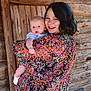 woman, baby, child, floral_dress, smile, portrait, outdoor, wooden_wall, holding, person, cute, infant, happy, family, love, casual, natural_light, skin, head, face