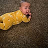 Aliyah is registered to the contest to win money with this photo: baby, child, infant, yellow_onesie, floral_pattern, carpet, brown_carpet, tummy_time, curious_expression, lying_down, indoors, cute, small_hands, face, head, young_child, person, childrens_clothing, floor, portrait