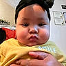 Aliyah is registered to the contest to win money with this photo: baby, child, face, headband, black_bow, yellow_shirt, hand, indoor, certificate, wall, plant, curious, chubby_cheeks, portrait, person, clothing, closeup, expression, skin, holding