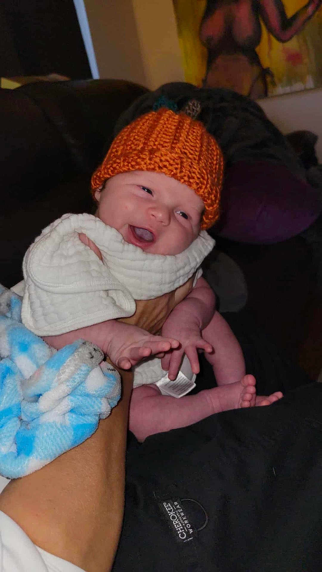 Dominic joined the competition — help win amazing prizes! baby, infant, smiling, knit_hat, blanket, hand, foot, adult_arm, white_cloth, blue_blanket, indoor, person, cute, happy, portrait, cozy, warm, cloth_tag, painting, dark_background